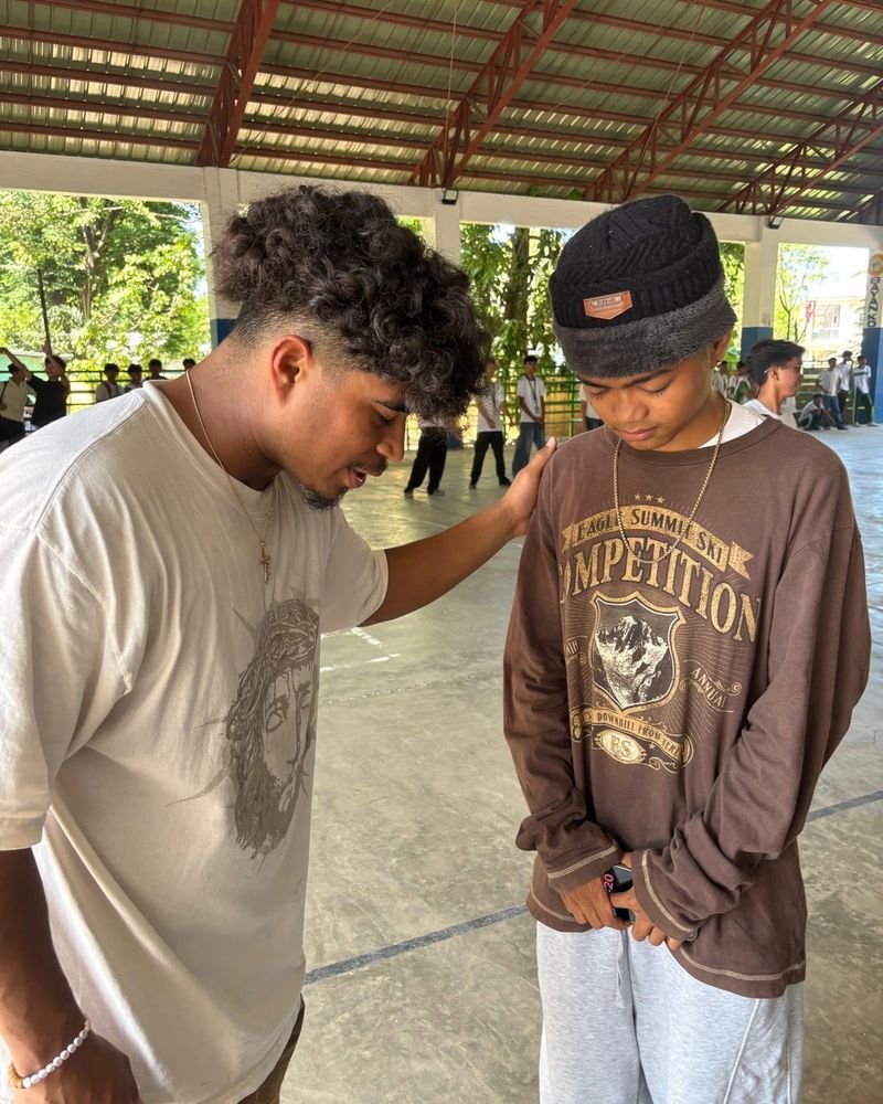 A young man praying with another, a hand resting on his shoulder